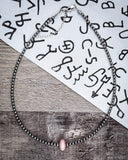 Necklace with a pink bead on a wooden surface with text in the background