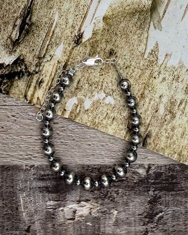Silver beaded bracelet on a wooden surface with a natural background