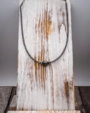 Silver beaded necklace on a rustic wooden surface with a gray background