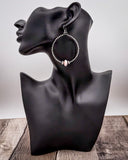 Black mannequin bust with hoop earrings on a wooden surface and light gray background