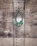 Beaded earring with green stones on a wooden surface with a ruler for scale.