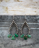 Pair of earrings with green teardrop-shaped turquoise stones on a textured surface