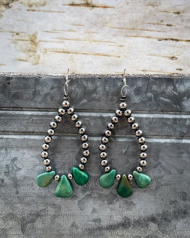 Pair of earrings with green teardrop-shaped turquoise stones on a textured surface