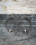 Pair of silver beaded hoop earrings on a textured metal surface