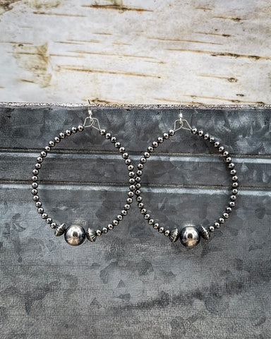 Pair of silver beaded hoop earrings on a textured metal surface