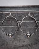 Pair of silver hoop earrings with beads hanging on a textured surface