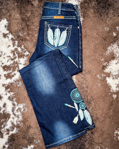 Blue jeans with feather and dreamcatcher designs on a textured brown surface