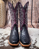 Purple and black ostrich cowboy boots on a textured surface