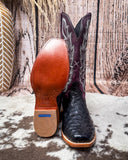 Purple and black ostrich cowboy boots on a textured surface