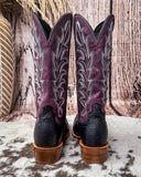 Purple and black ostrich cowboy boots on a textured surface