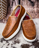 Pair of brown leather loafers with white soles on a textured surface