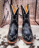 Pair of black cowboy boots with white stitching on a wooden surface.