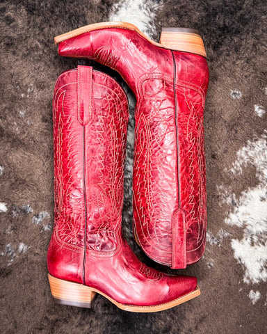 Red cowboy boots with intricate patterns on a textured surface