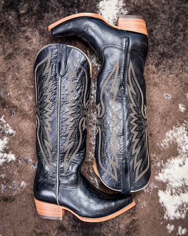 Pair of black cowboy boots with intricate copper embroidery on a textured surface