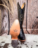 Black cowboy boot with intricate design on a wooden background