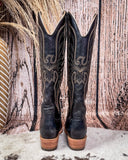 Pair of black cowboy boots with intricate copper embroidery on a textured wooden background