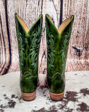 Pair of green cowboy boots with intricate designs on a wooden background