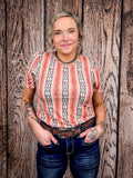 Smiling woman modeling peach and navy Aztec top with ruched shoulders and statement earrings.