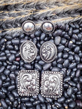Set of three western stud earrings—round, oval, and square—on rustic black bean and wheat backdrop
