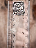 Rectangular silver stud earring with floral scroll engraving and beaded edge shown on ruler