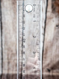 Small silver stud earring with rope border shown on clear ruler for size reference