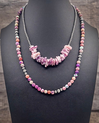 A double-strand necklace displayed on a black jewelry bust. One strand features polished pink and purple stone beads with small silver spacer beads, while the other strand has a central cluster of irregular pink stone chips flanked by silver-toned beads.