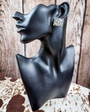Trailblazer Concho Fashion Stud square earring on a mannequin, sitting on cowhide, wood back drop. 