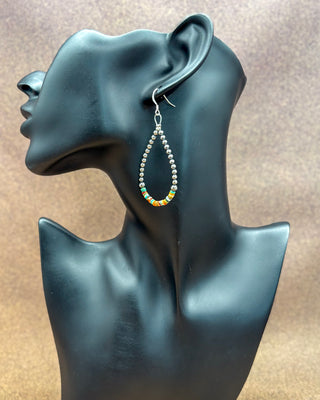 A pair of silver-toned beaded teardrop dangle earrings with small multicolor bead accents, displayed on a black mannequin bust against a textured brown background.