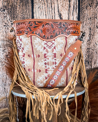 Front view of the Trial Hand-Tooled Bag displayed on a wood table, wood back drop.