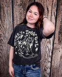 Girl modeling the Honky Tonk Gal Vintage Graphic Tee with a wood back drop.