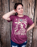A girl modeling the Adios Cowboy Distressed Graphic Tee with a wood back drop.