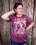 A girl modeling the Adios Cowboy Distressed Graphic Tee with a wood back drop.