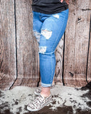 A girl modeling the Coyote Trail High-Rise Mom Jeans on cowhide, wood backdrop.