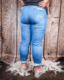 Back view of a girl modeling the Coyote Trail High-Rise Mom Jeans while on cowhide, wood back drop.
