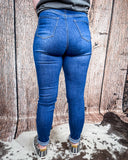 Back view of a girl wearing the Badlands Rip Skinny Jeans while standing on cowhide, wood back drop.