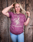 A girl modeling the Urban Cowboy Distressed Graphic Tee with a wood back drop.