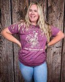 A girl modeling the Urban Cowboy Distressed Graphic Tee with a wood back drop.