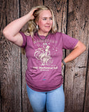 A girl modeling the Urban Cowboy Distressed Graphic Tee with a wood back drop.