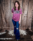 A model wearing the Lightning Cowgirl Distressed Graphic Tee with a wood back drop on cowhide.