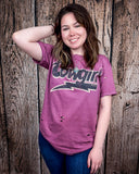 A model wearing the Lightning Cowgirl Distressed Graphic Tee with a wood back drop.