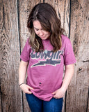 A model wearing the Lightning Cowgirl Distressed Graphic Tee with a wood back drop.