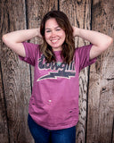 A model wearing the Lightning Cowgirl Distressed Graphic Tee with a wood back drop.