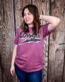 A model wearing the Lightning Cowgirl Distressed Graphic Tee with a wood back drop.