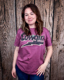 A model wearing the Lightning Cowgirl Distressed Graphic Tee with a wood back drop.