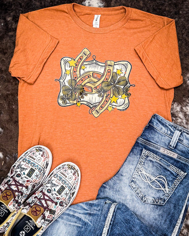 The Lucky Stars Graphic Tee displayed on cowhide along with shoes and jeans.