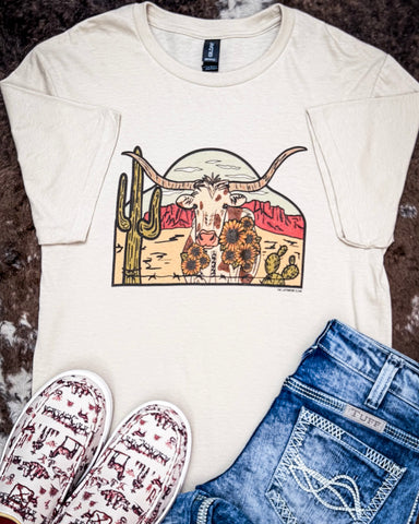 Front view of the The Laredo Longhorn Graphic Tee displayed on cowhide along with shoes and jeans.