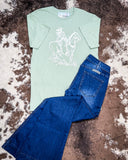 The Legacy Rider Graphic Tee displayed on cowhide along with jeans.