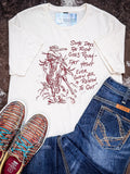 The Still in The Saddle Graphic Tee displayed on cowhide along with shoes and jeans.