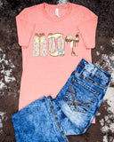The Blooming Cowgirl Essentials Graphic Tee displayed on cowhide along with jeans.