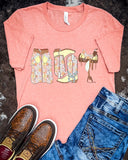 The Blooming Cowgirl Essentials Graphic Tee displayed on cowhide along with jeans and shoes.